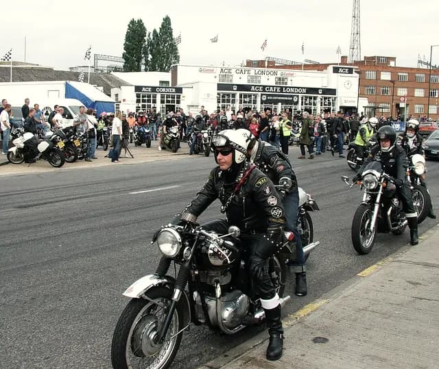 Leather-jacketed riders on vintage British motorcycles pulling out from the Ace Cafe in London